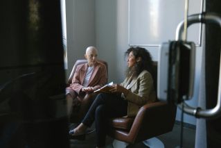 Young female colleagues in trendy outfits sitting in armchairs and talking in meeting room